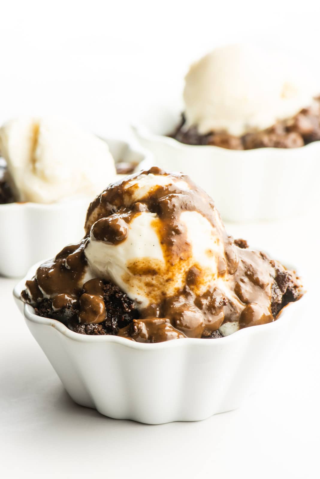 Three dessert bowls hold chocolate cake topped with ice cream. The main one has chocolate sauce over the top.