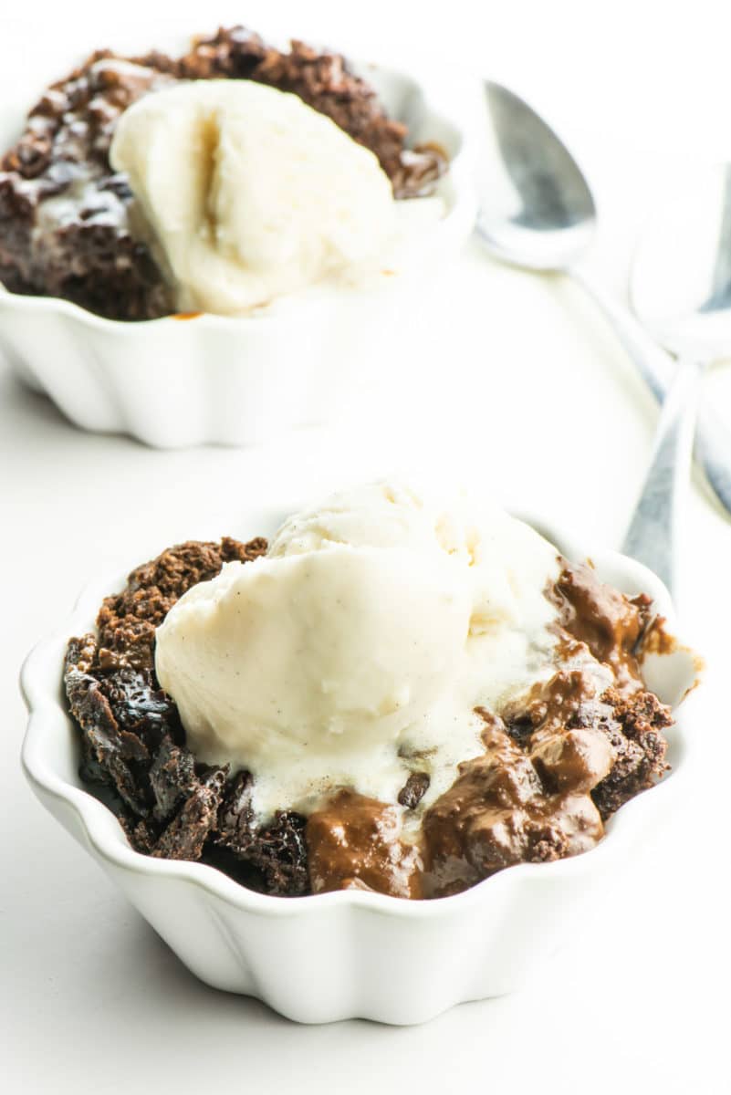 Two bowls hold chocolate pudding cake topped with ice cream with spoons between them.