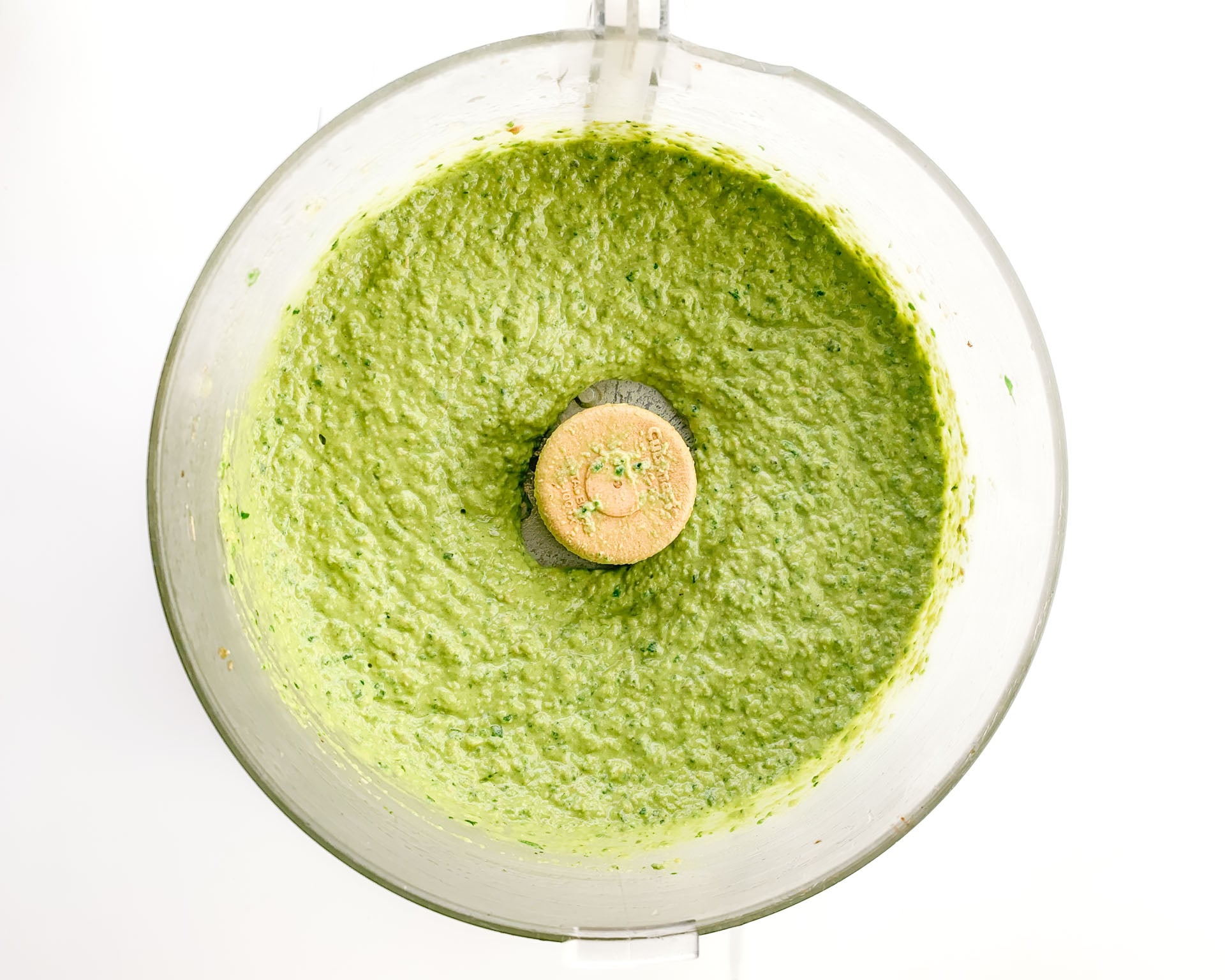 Green hummus in a food processor after being pulsed.