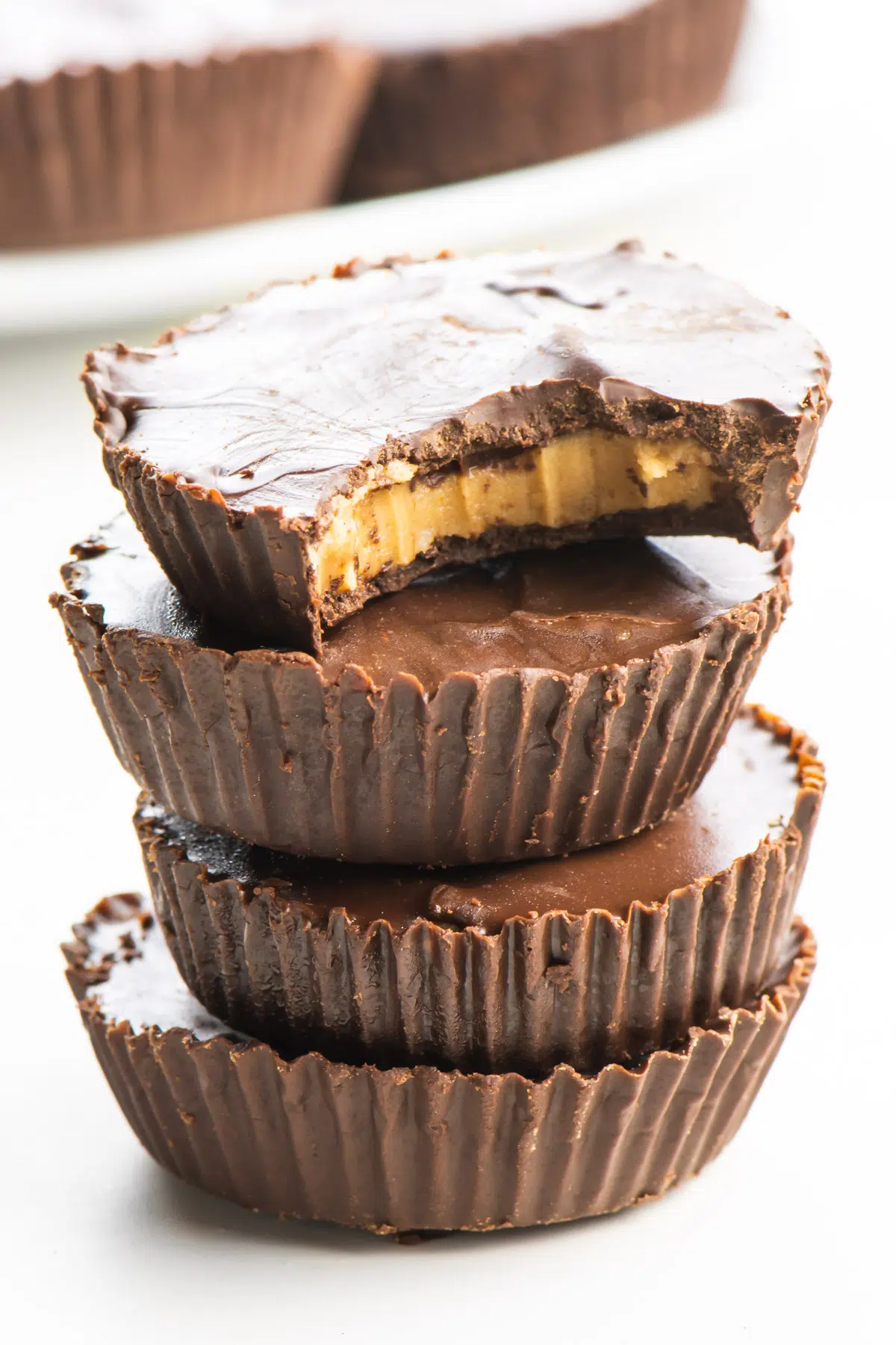 A stack of several vegan peanut butter cups, the top one with a bite taken out.