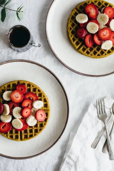 Looking down on two plates with waffles topped with fresh fruit.
