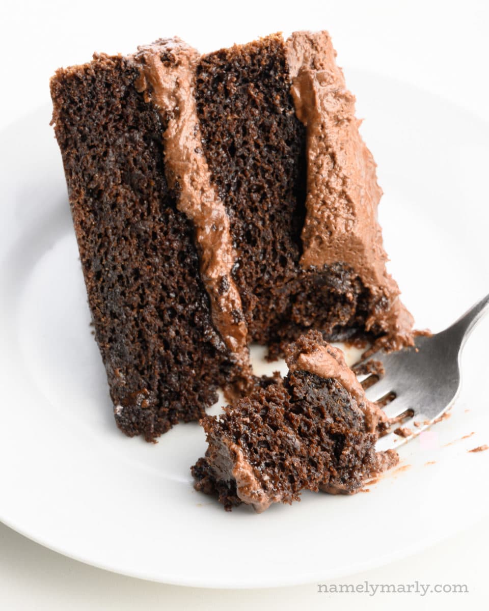 A slice of chocolate cake sits on its side with a bite cut out with a fork.
