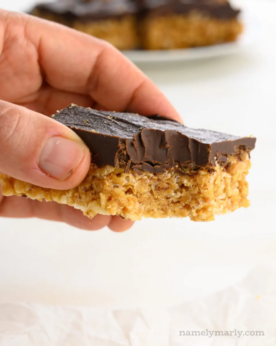 A hand holds a peanut butter rice krispies treat with a bite taken out of it.