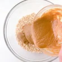 Peanut butter sauce is being poured over a bowl of rice krispies cereal.