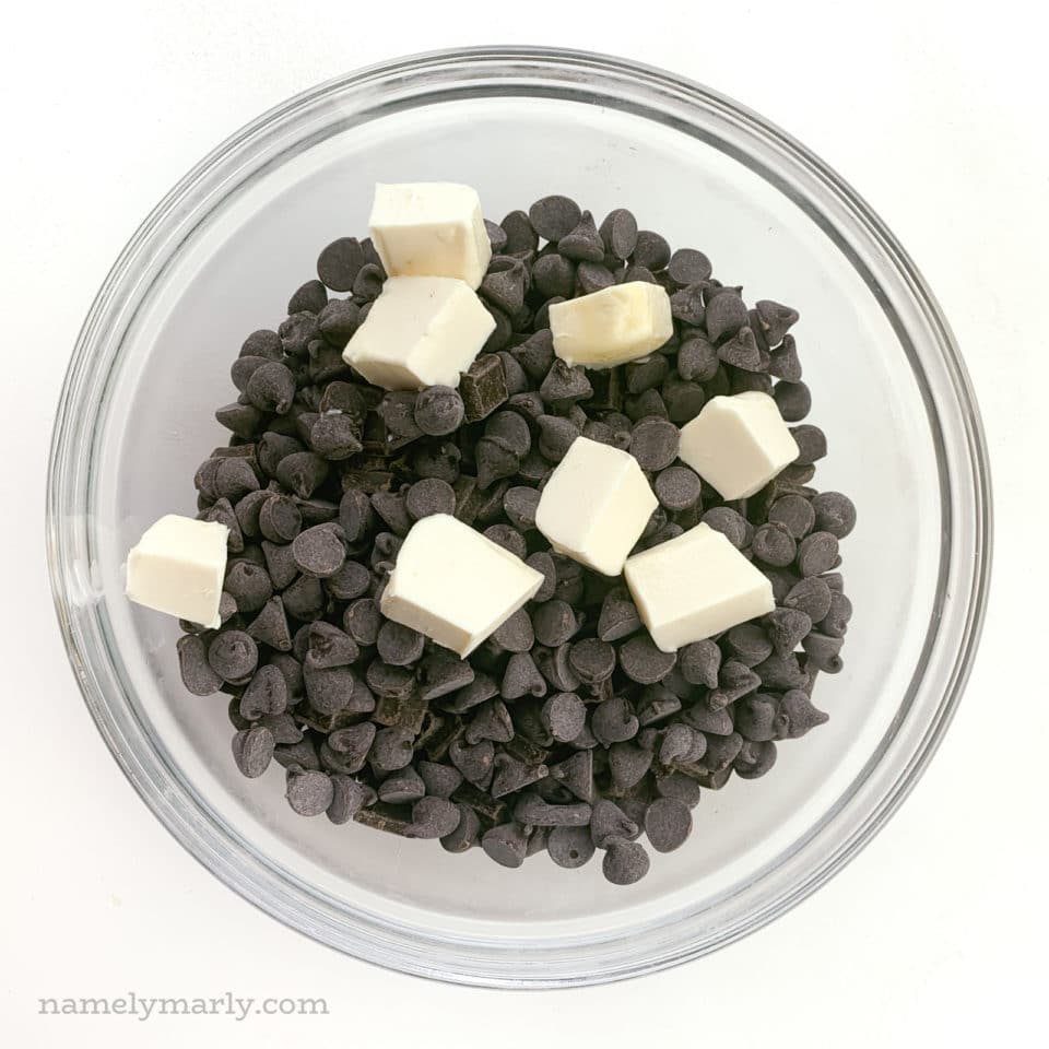 Cubes of vegan butter are sitting on top of chocolate chips in a glass bowl.