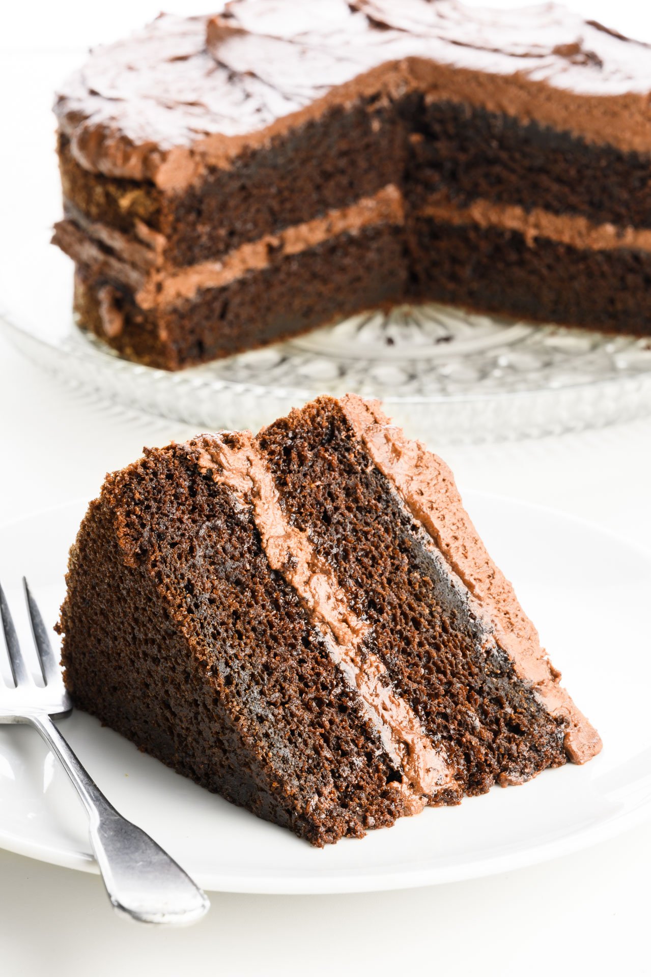 A slice of cake on a plate with a fork beside it sits in front of the rest of the cake.