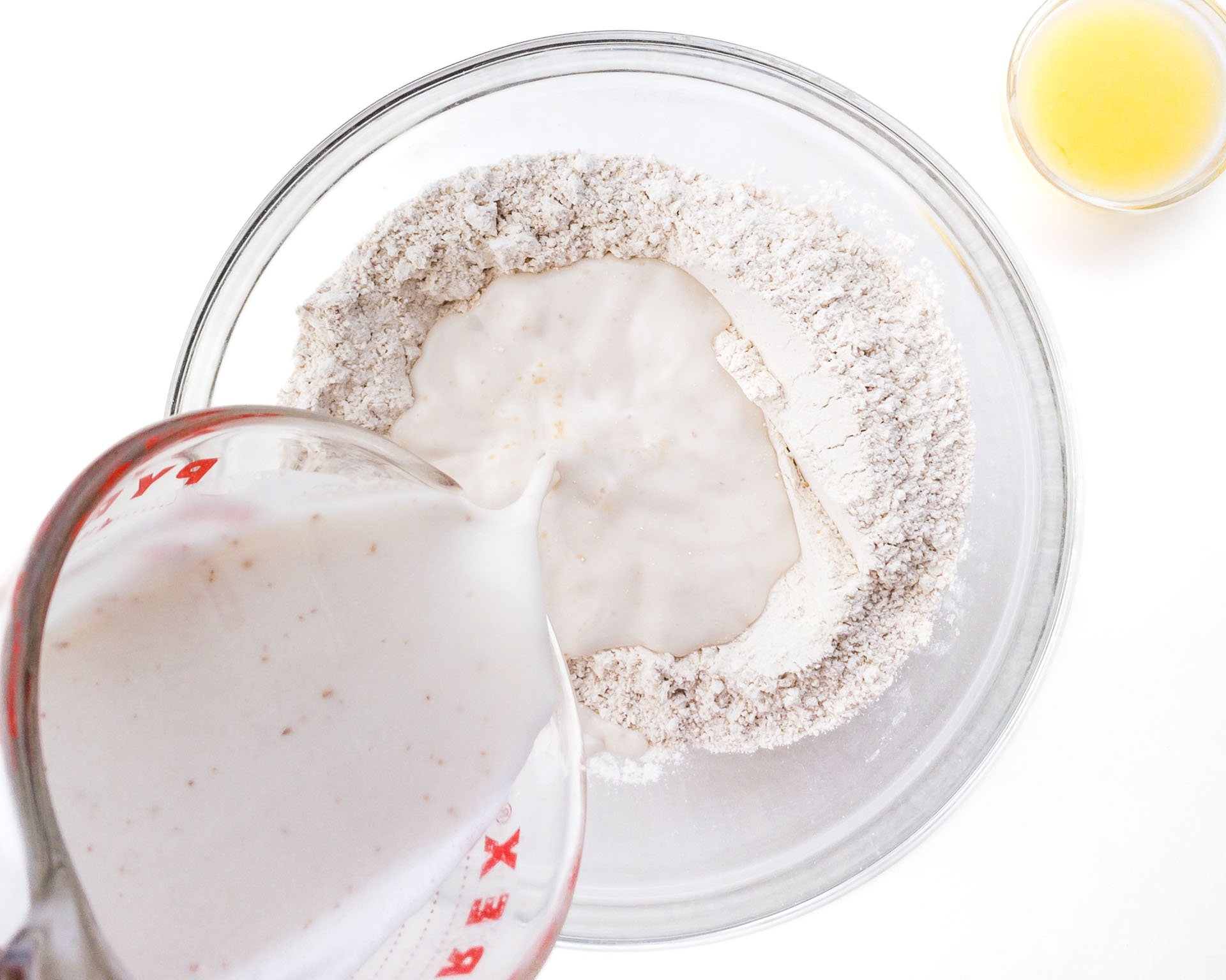 Plant-based milk is being poured from a measuring cup into a bowl with the flour mixture.