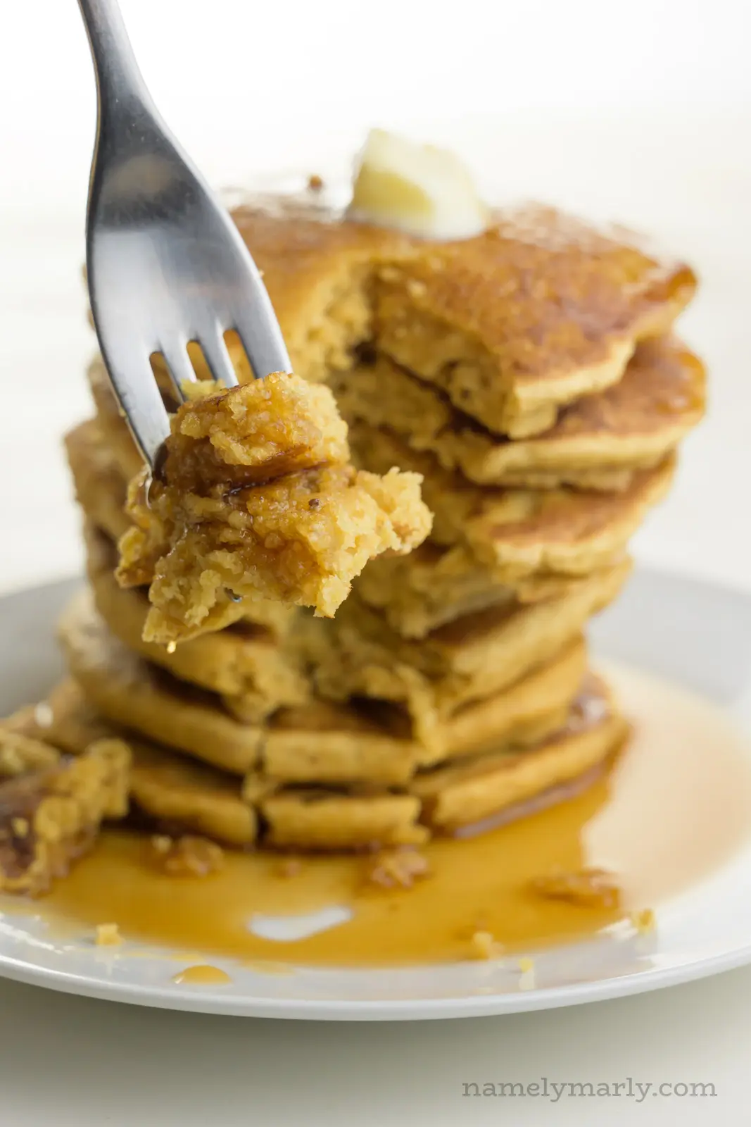 A fork holds a bite of pancakes in front of the rest of the plateful.