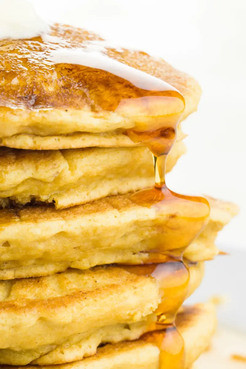 A close-up photo of a tall stack of pancakes, showing maple syrup following over the edges.