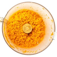 Grated carrots are in the bottom of a food processor bowl.