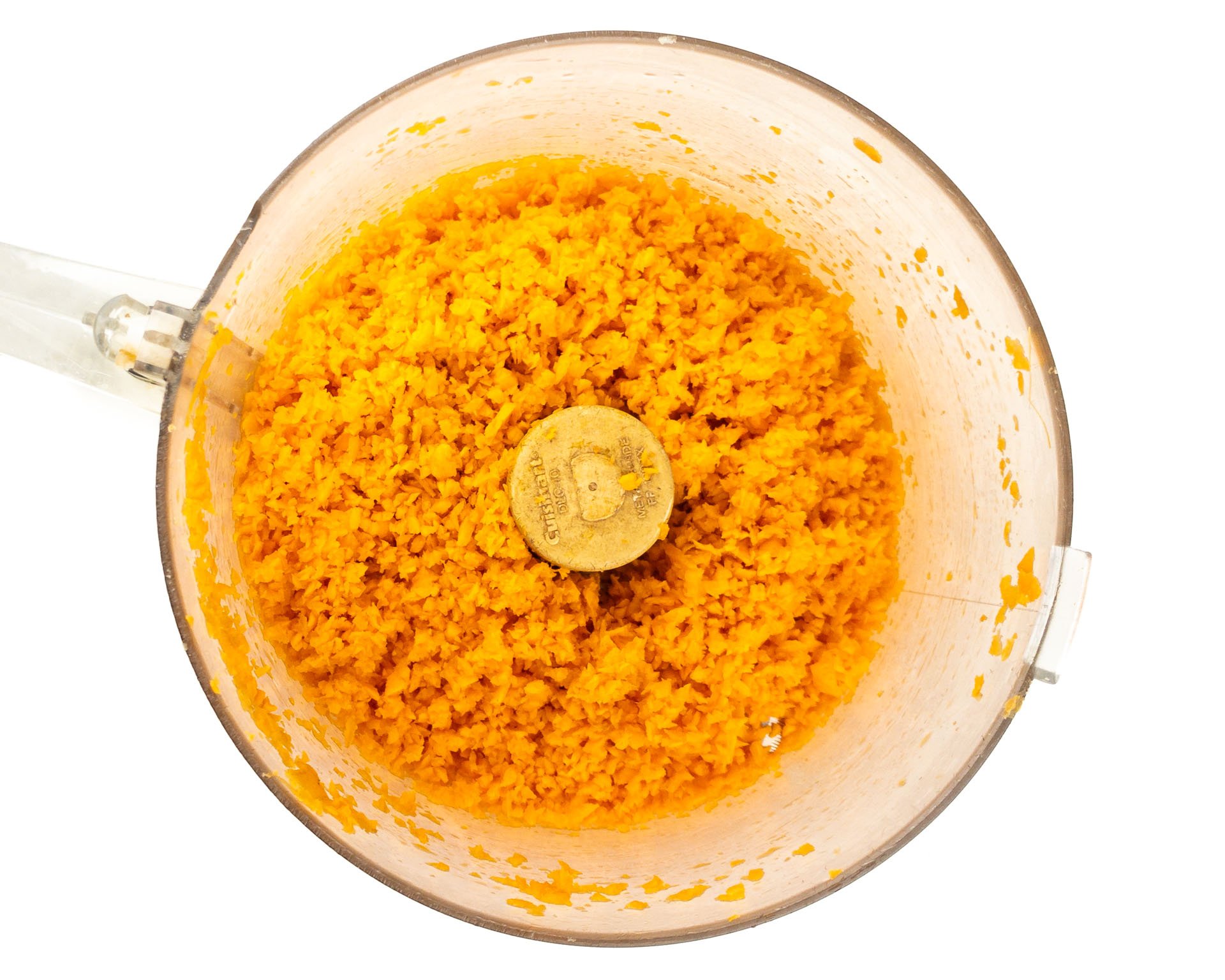 Grated carrots are in the bottom of a food processor bowl.