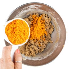 Carrots are being added to cookie batter in a mixing bowl.