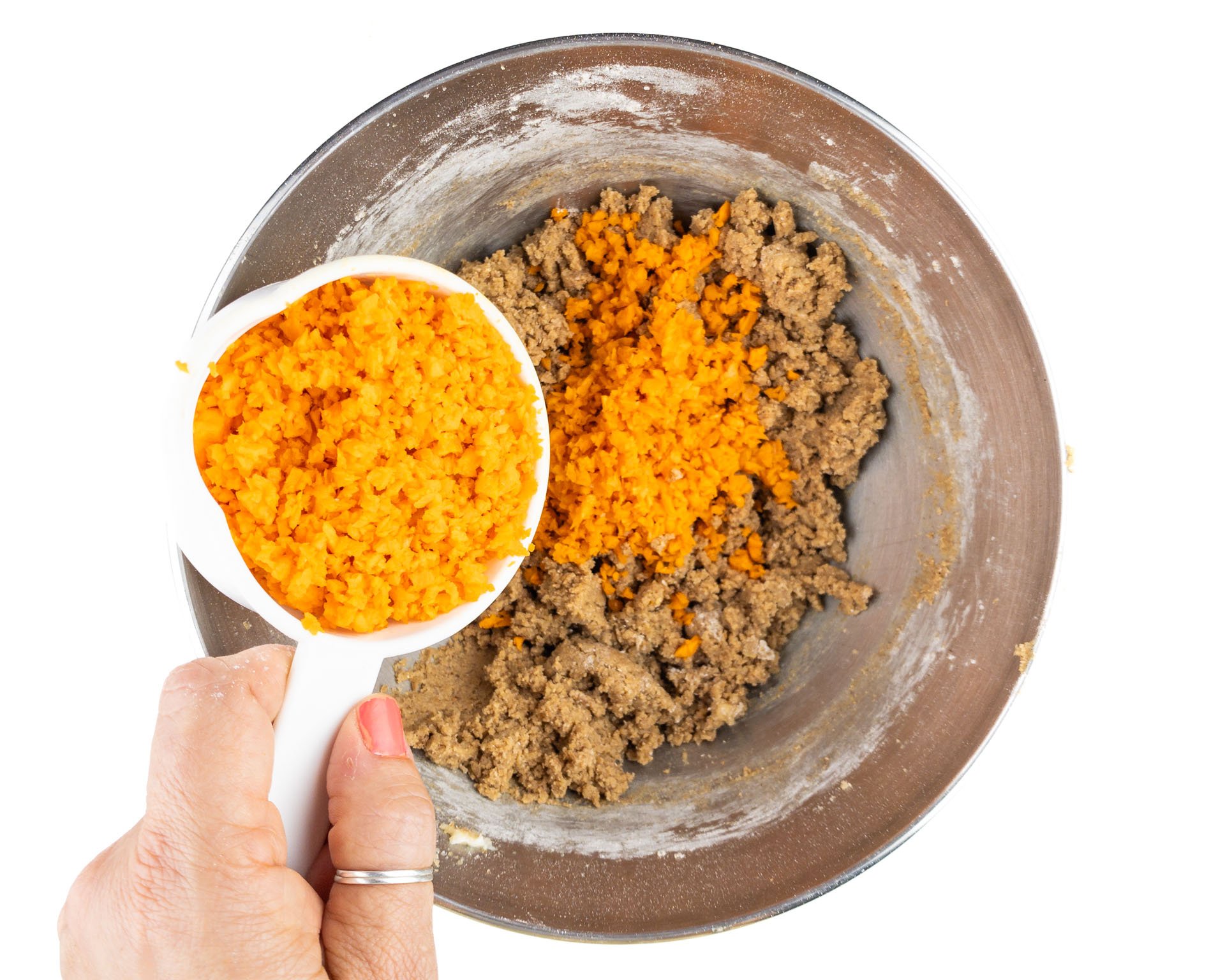Carrots are being added to cookie batter in a mixing bowl.