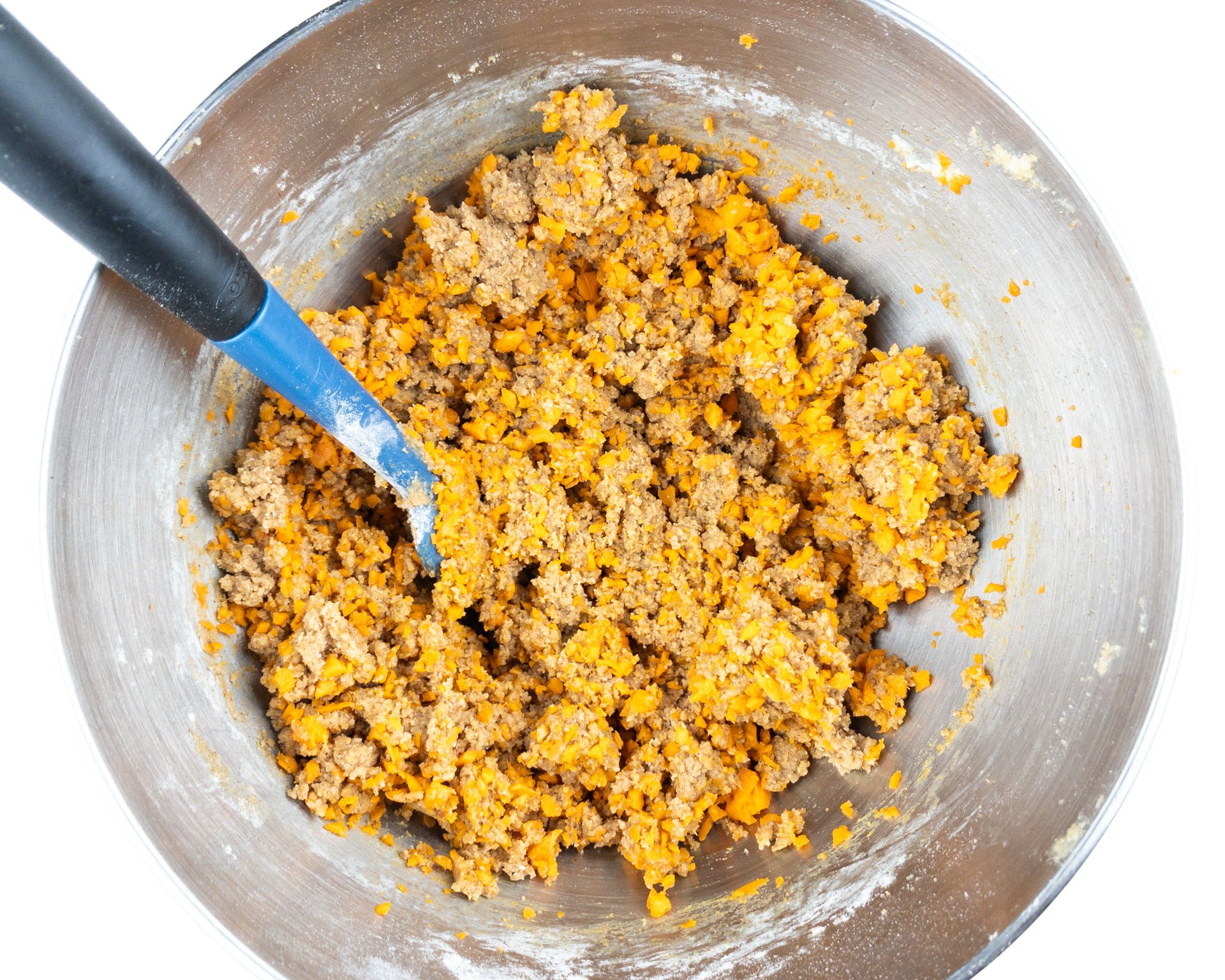 Cookie dough batter in the bottom of a mixing bowl with a spatula for stirring it.