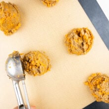 A cookie dough dispenser is being used to drop cookie dough balls on a cookie sheet.