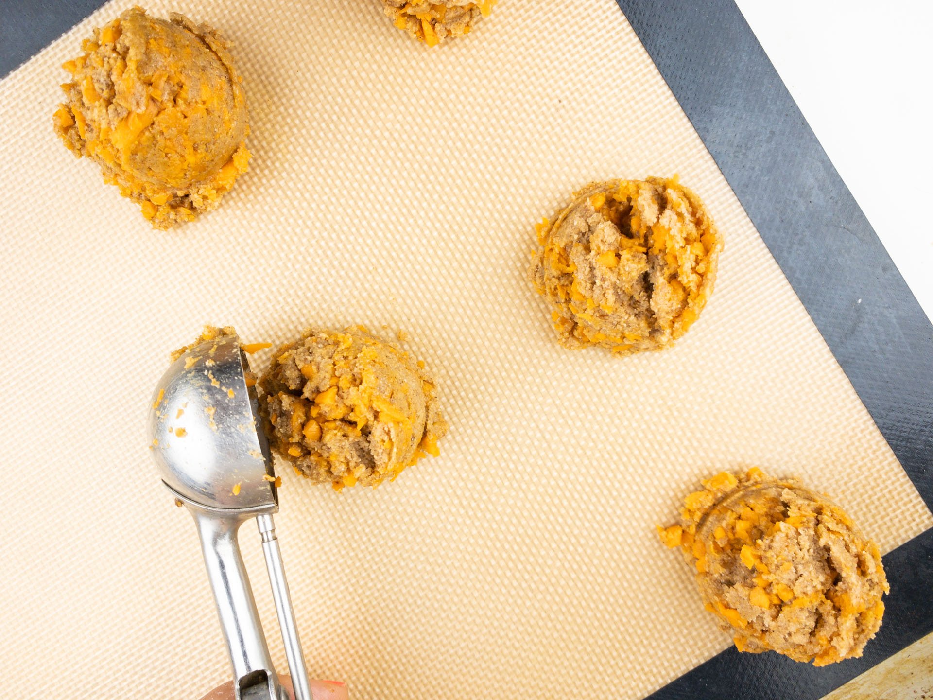 A cookie dough dispenser is being used to drop cookie dough balls on a cookie sheet.