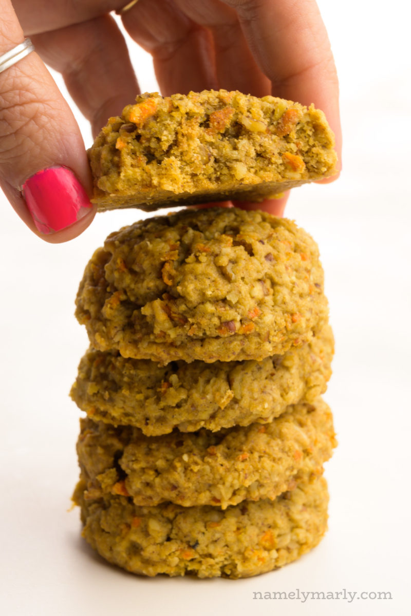 A hand grabs the top cookie from the stack of several unfrosted cookies.