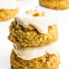 A stack of frosted carrot cake cookies sits in front of more cookies.