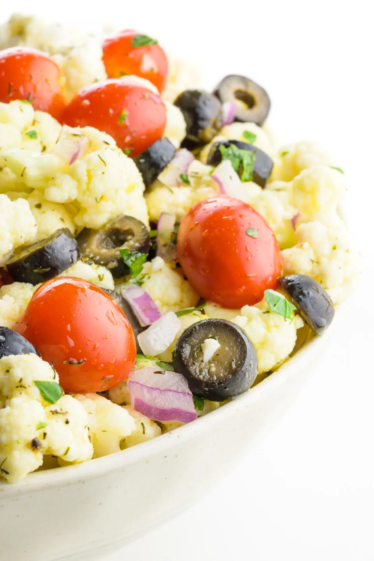 A closeup of a bowl featuring vegetables, such as cherry tomatoes, black olives, and cauliflower florets.