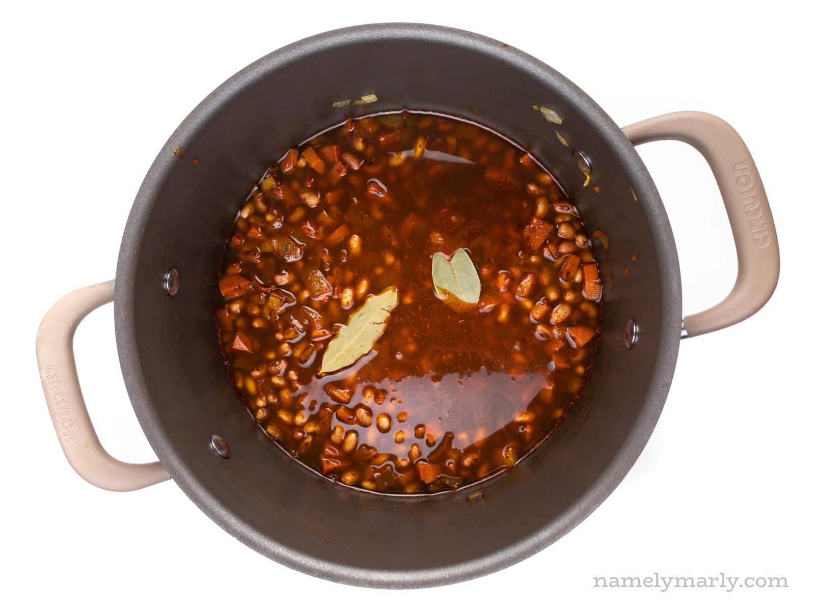 Looking down on a pot full of beans and broth with a couple of bay leaves on top.