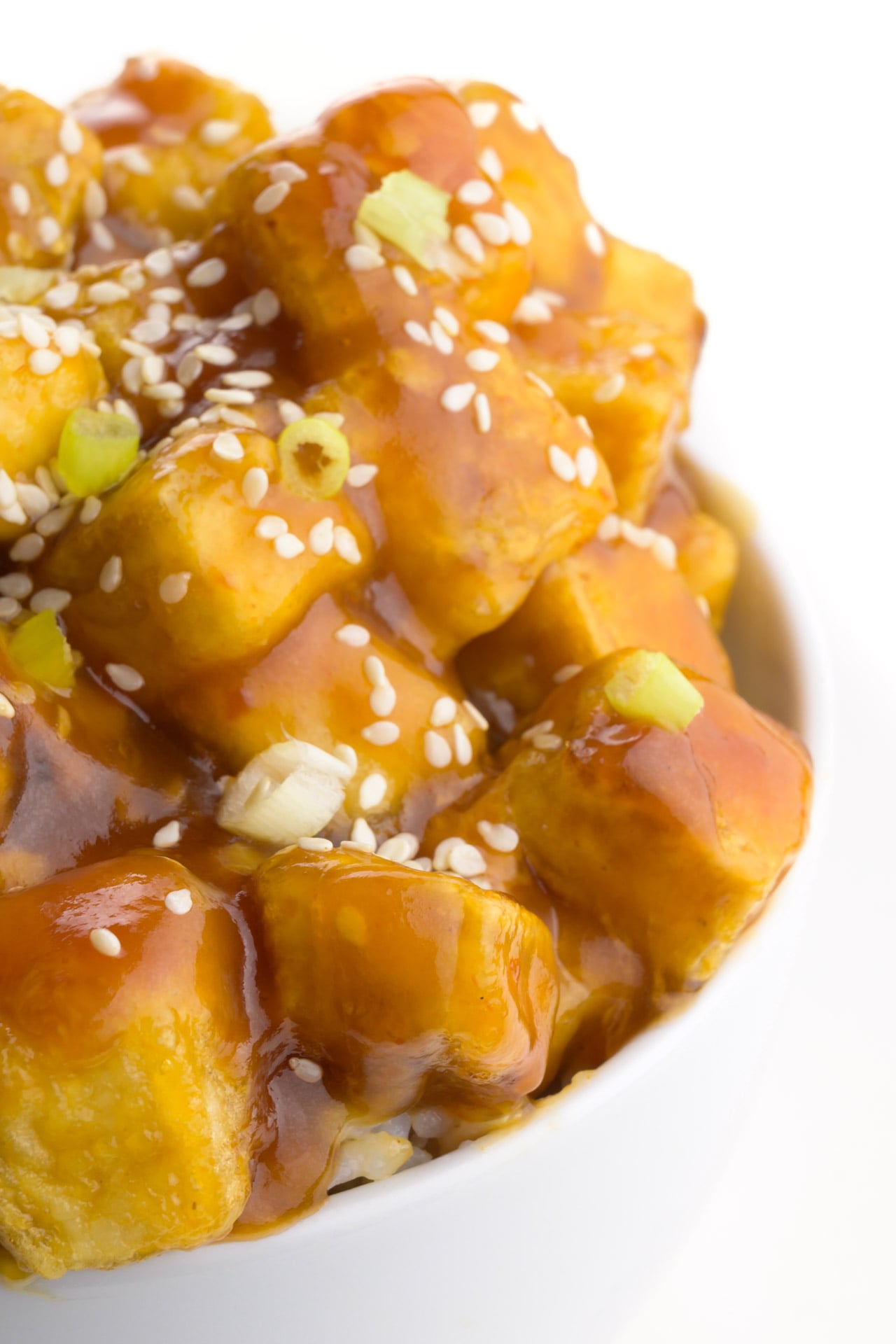 A closeup shot of a bowl of Asian tofu recipe with chopped green onions on top.