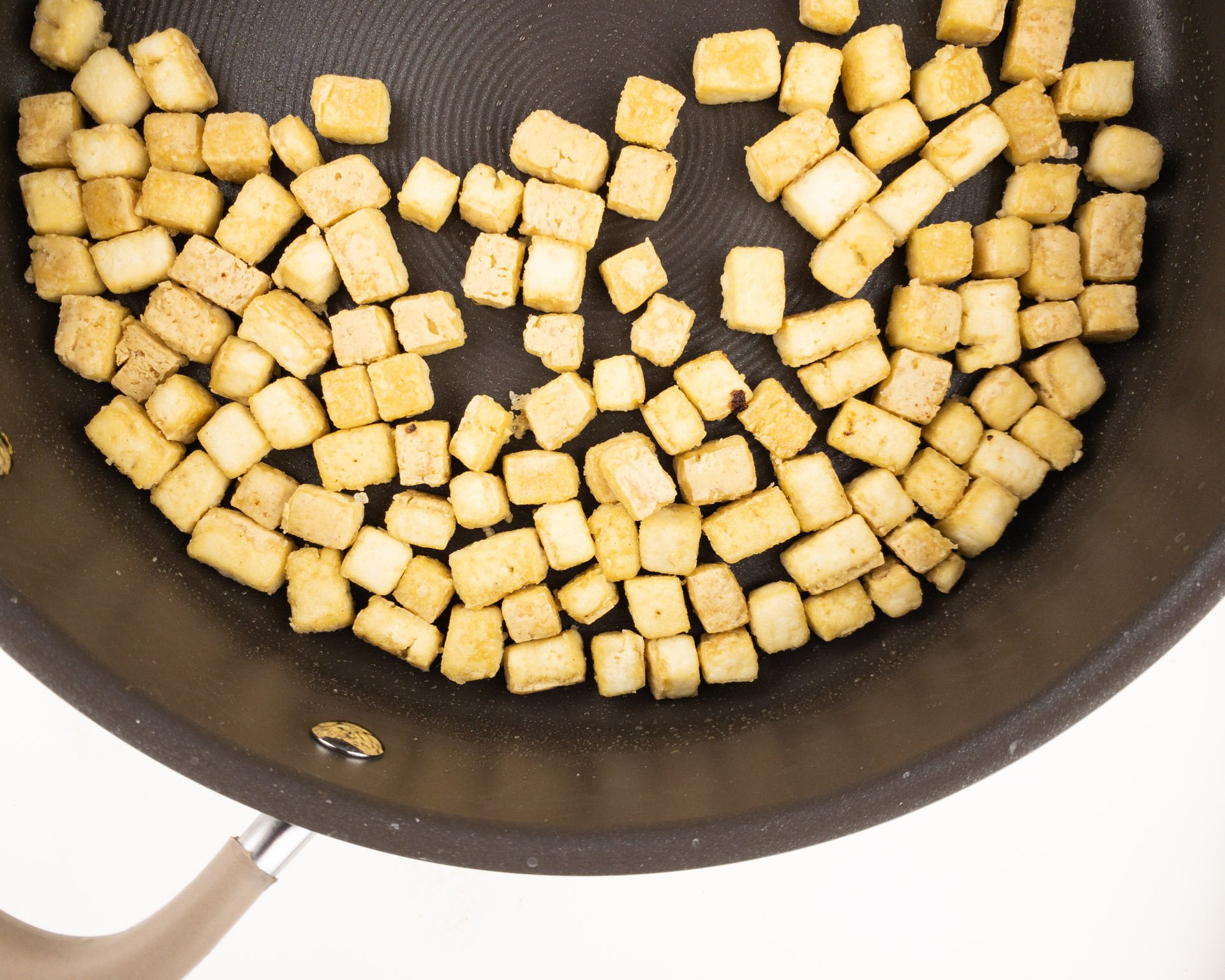 Cubes of tofu are being fried in a skillet.