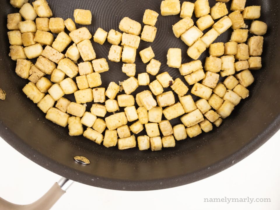 Cubes of tofu are being fried in a skillet.