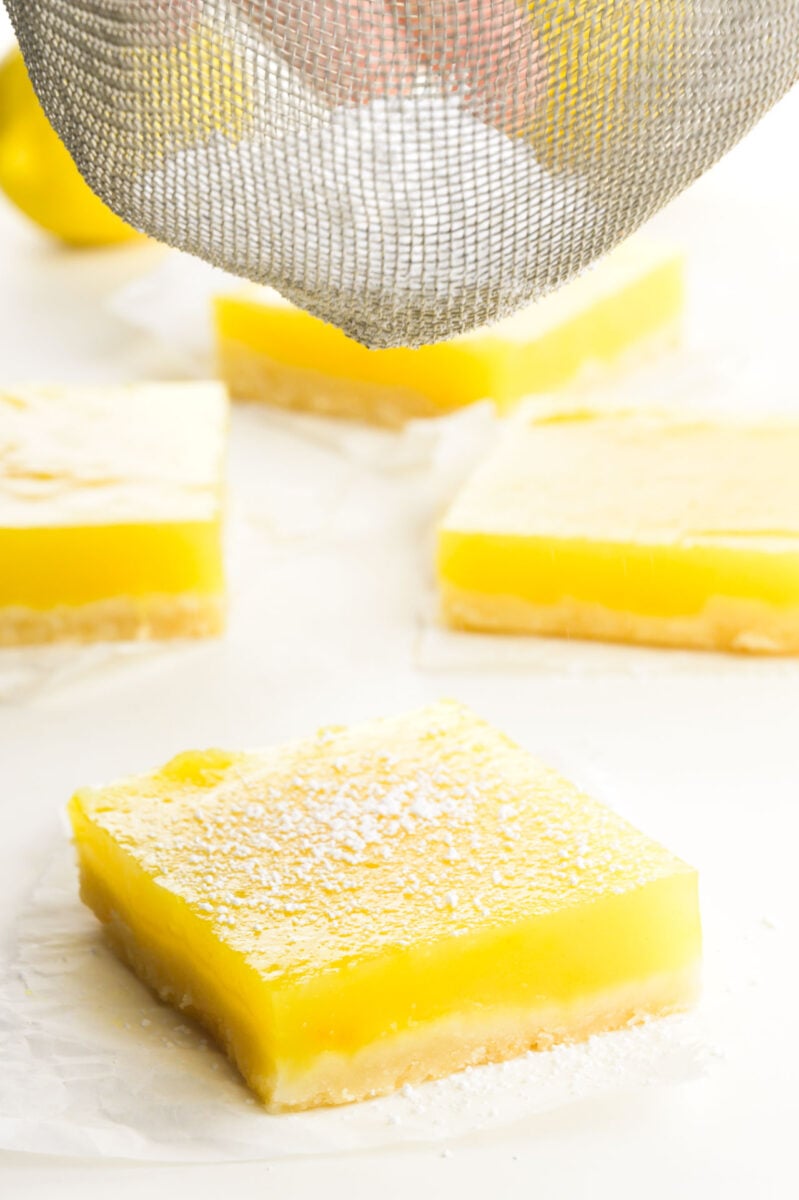 Powdered sugar is being sprinkled on cut dessert bars.