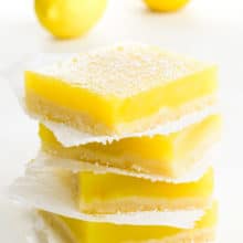 A stack of several lemon bars with two lemons behind it.
