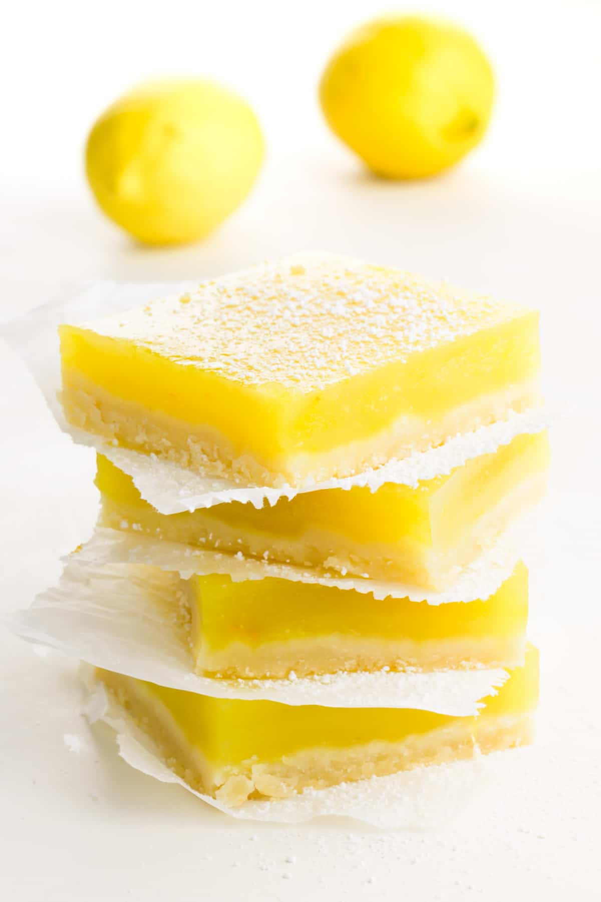 A stack of several lemon bars with two lemons behind it.