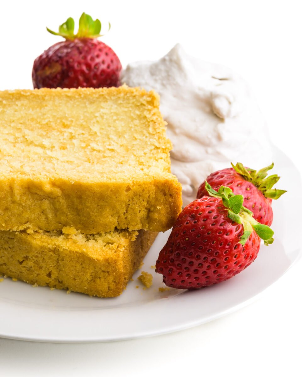 Two slices of pound cake are on a plate with strawberries and whipped cream.