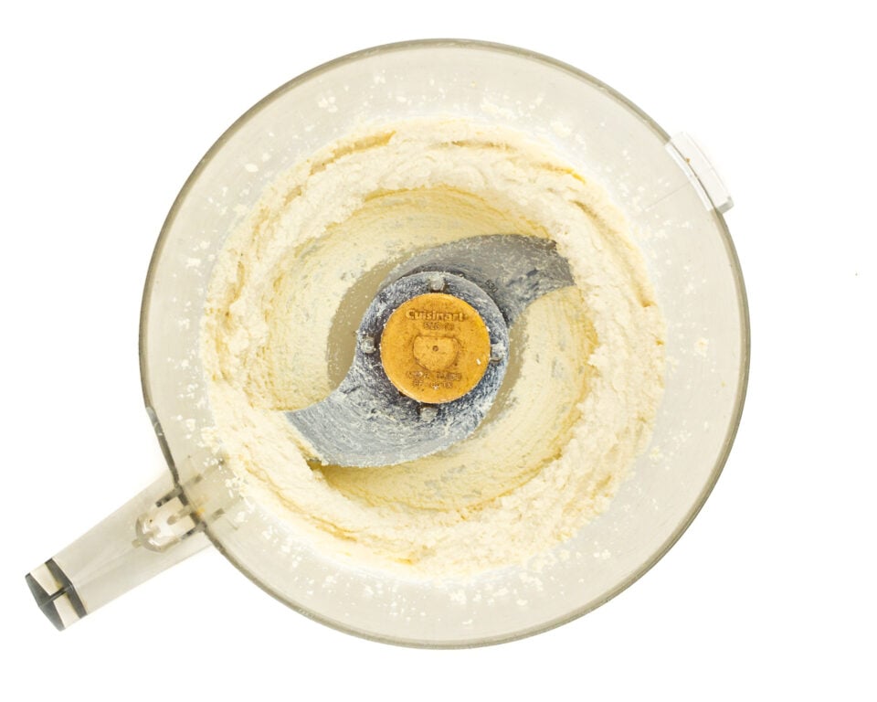 Whipped tofu is in the bottom of a food processor bowl.