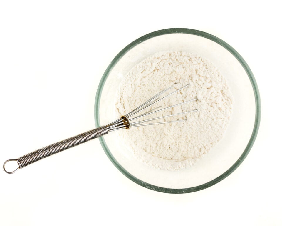 A wire whisk is in a bowl of flour mixture.