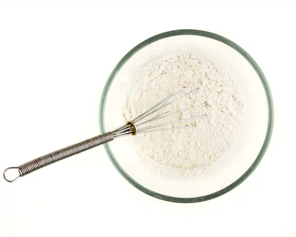 A wire whisk is in a bowl of flour mixture.
