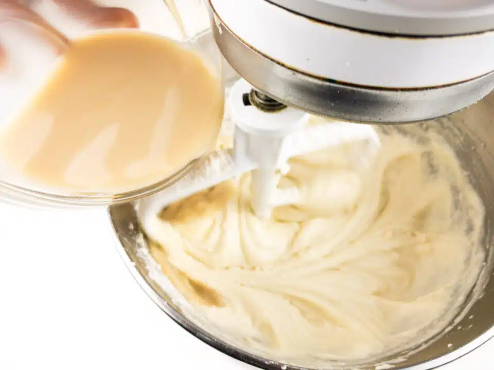 A vanilla-infused plant-based milk mixture is being poured into a stand mixture with a creamy batter.