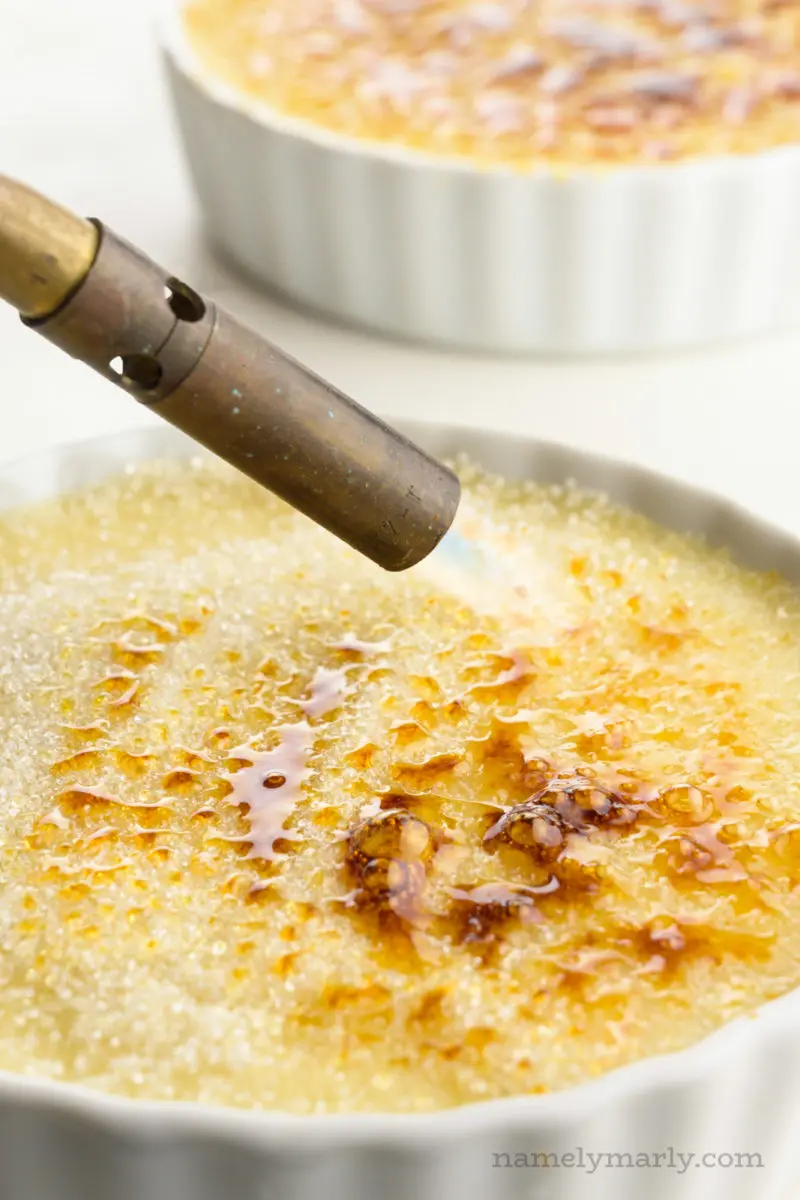 A torch has a flame going and is burning the sugar layer over creme brûlée.