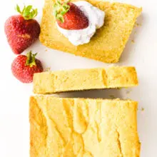 A slice of poundcake has whipped cream and strawberries on it with the rest of the pound cake loaf beside it.