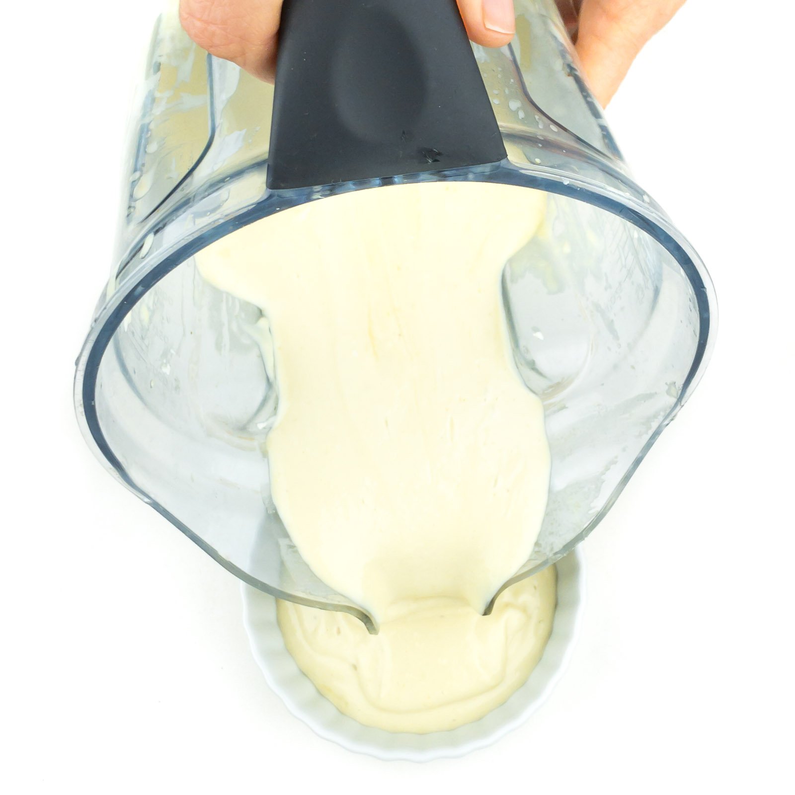 A creme sauce is being poured from a blender jar into a ramekin.