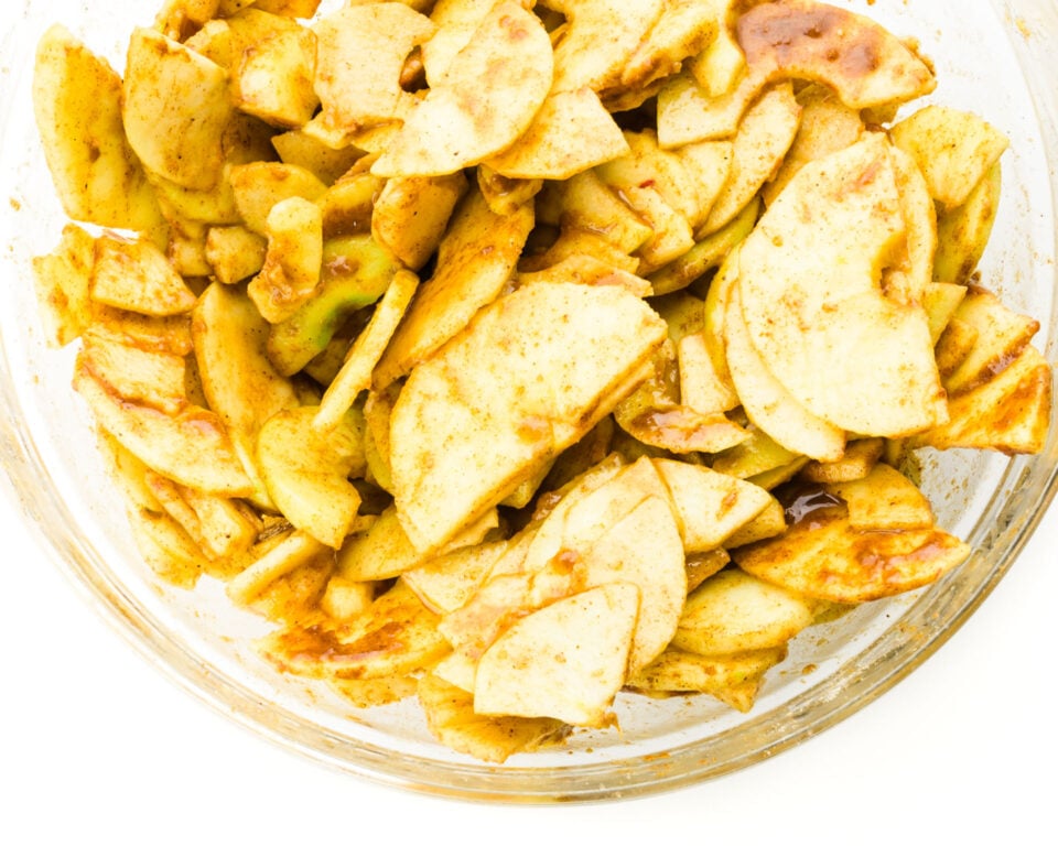 A bowl of sliced apples are drenched with cinnamon topping.