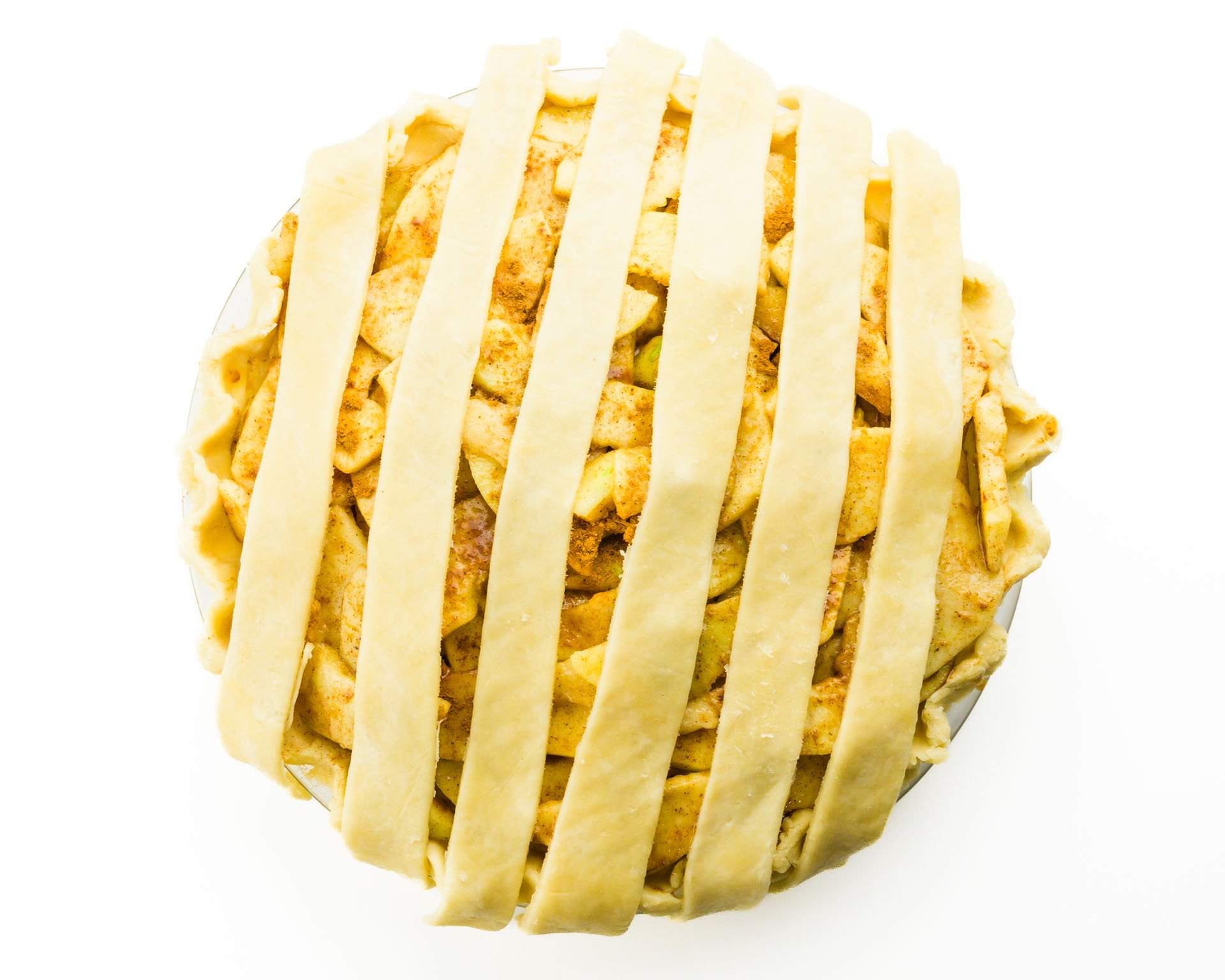Looking down on an unbaked apple pie with 6 strips of pie dough, preparing for the lattice topping.