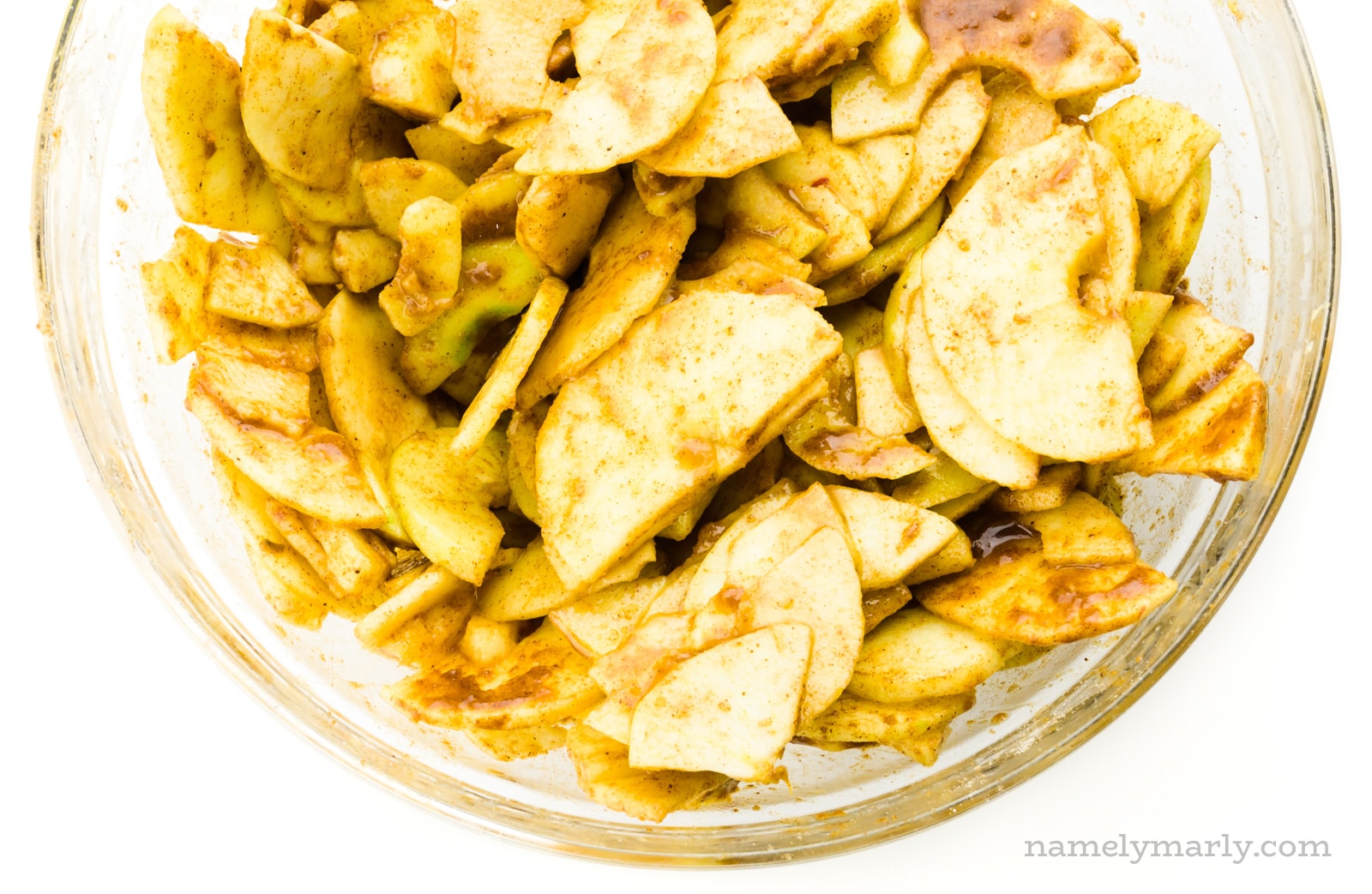 A bowl of sliced apples are drenched with cinnamon topping.