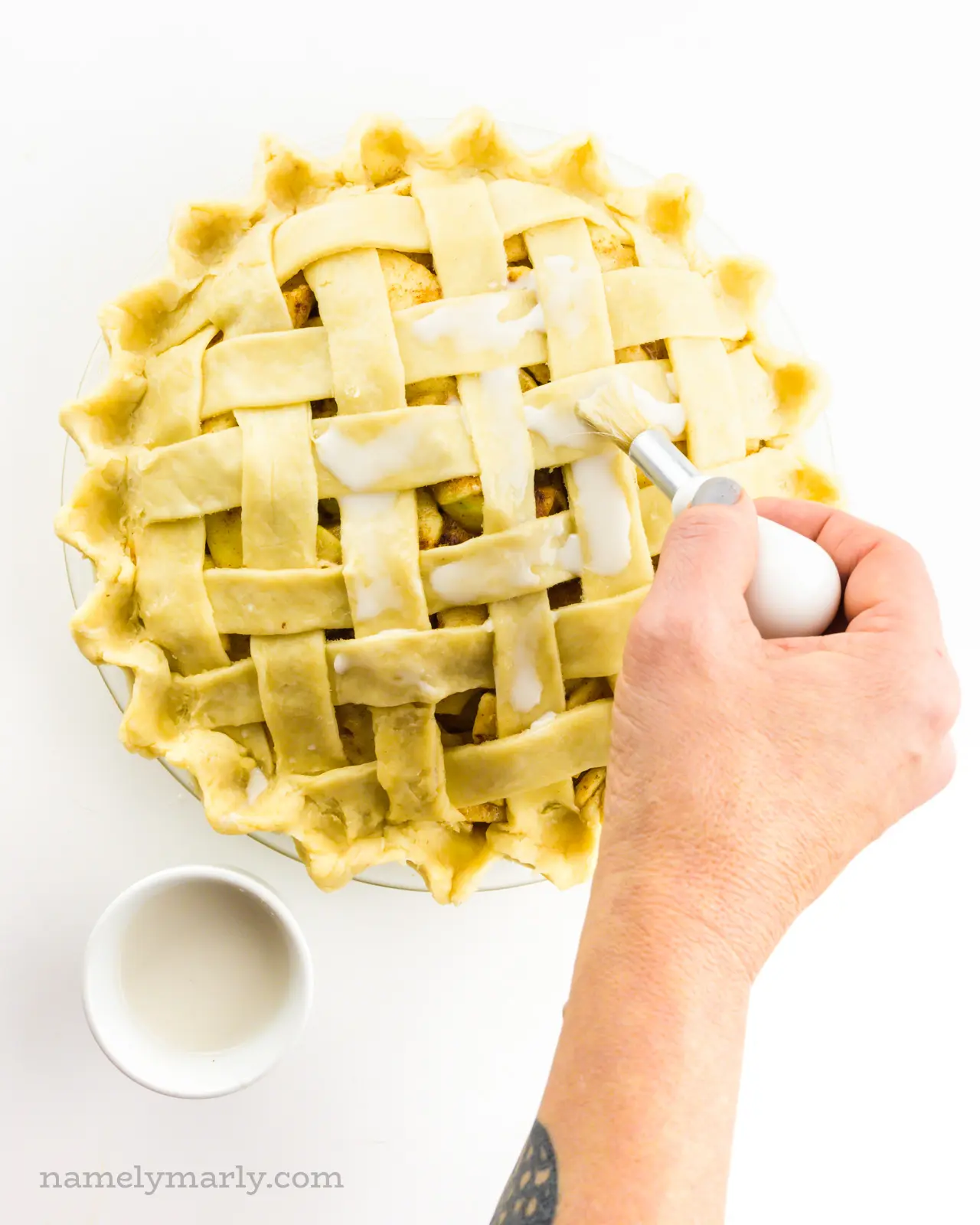 A hand holds a brush, adding vegan egg was to the unbaked pie crust.