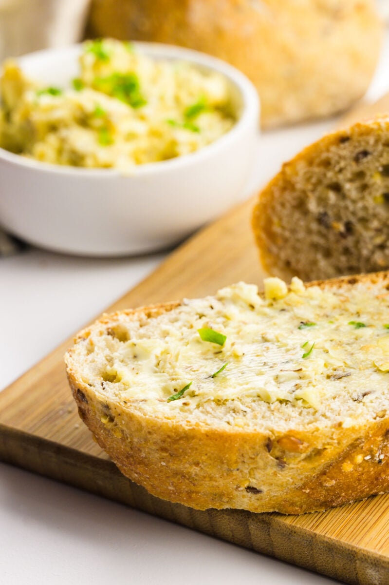 A slice of vegan garlic bread sits in front of garlic butter and more slices of bread.