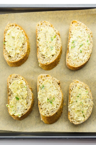 Looking down on several slices of buttered bread ready to go into the oven.