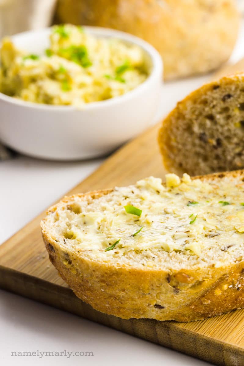 A slice of vegan garlic bread sits in front of garlic butter and more slices of bread.