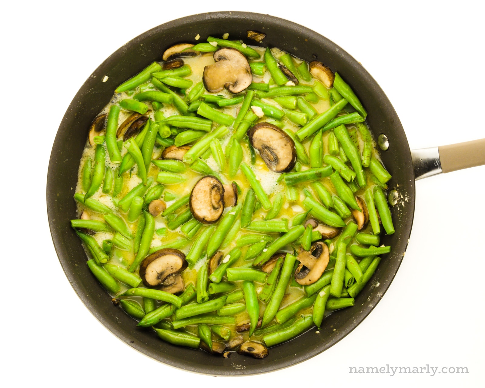 A skillet is full of green beans and mushrooms cooking.
