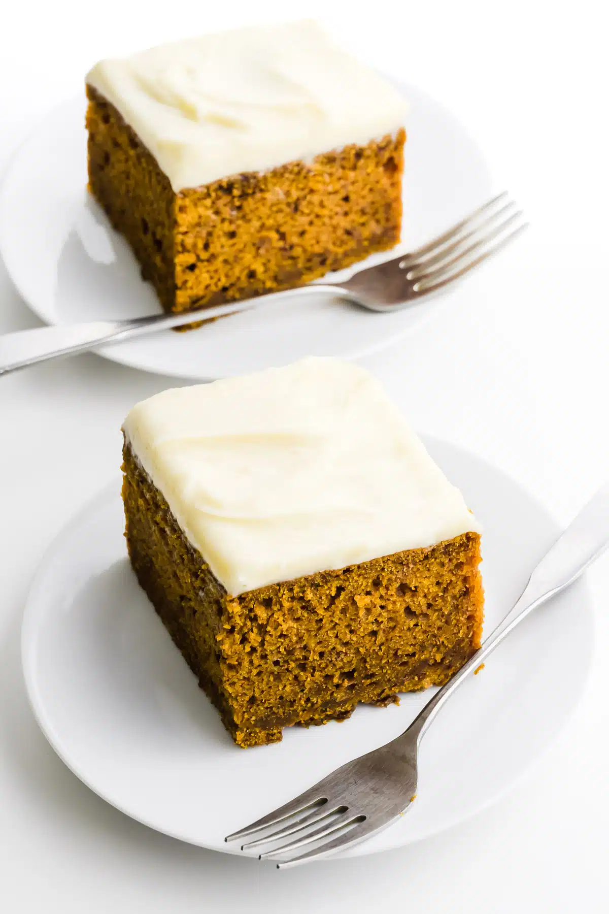Two slices of pumpkin spice cake are on plates with forks beside them.