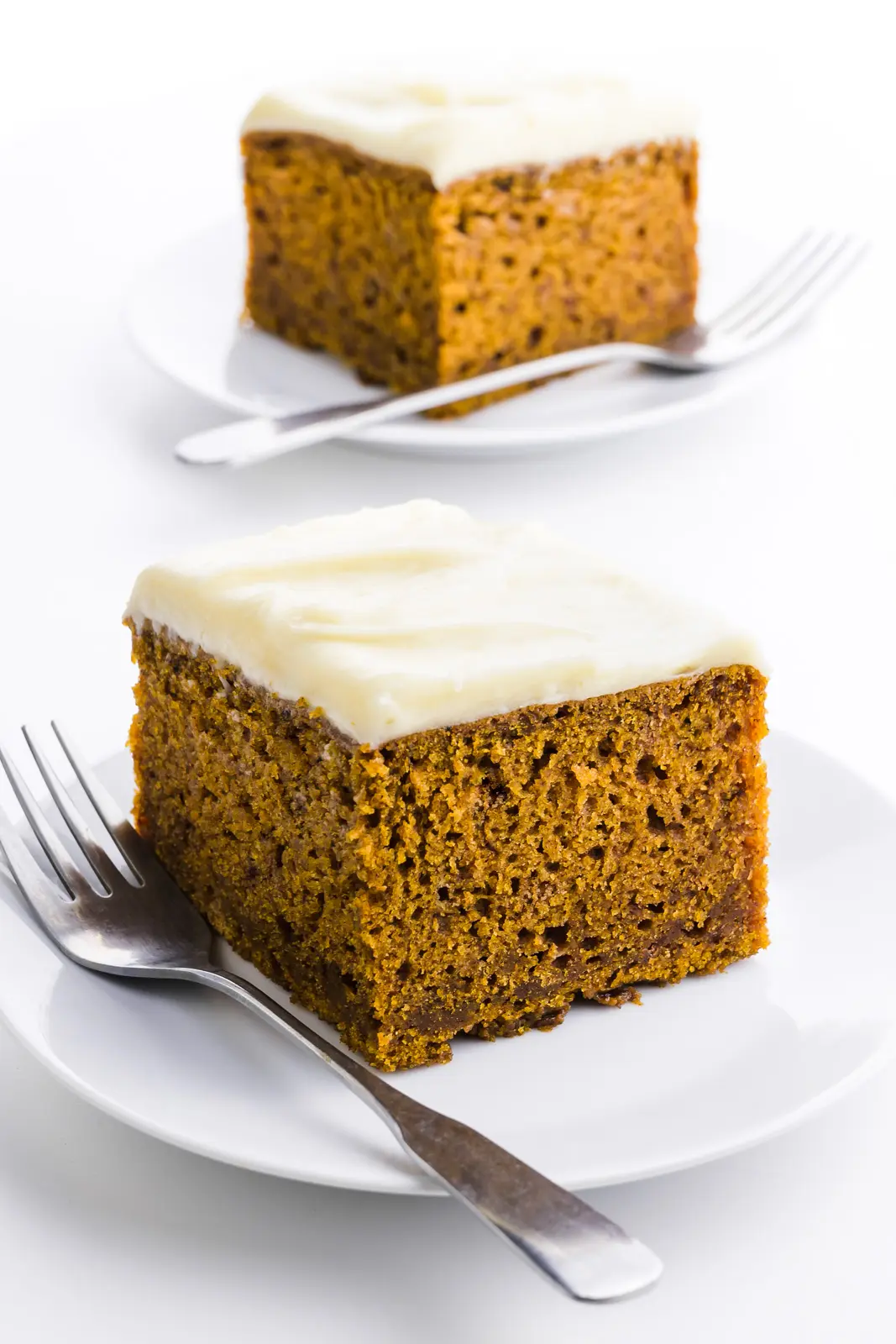 Two slices of pumpkin cake , one in front of the other, with forks beside each slice.