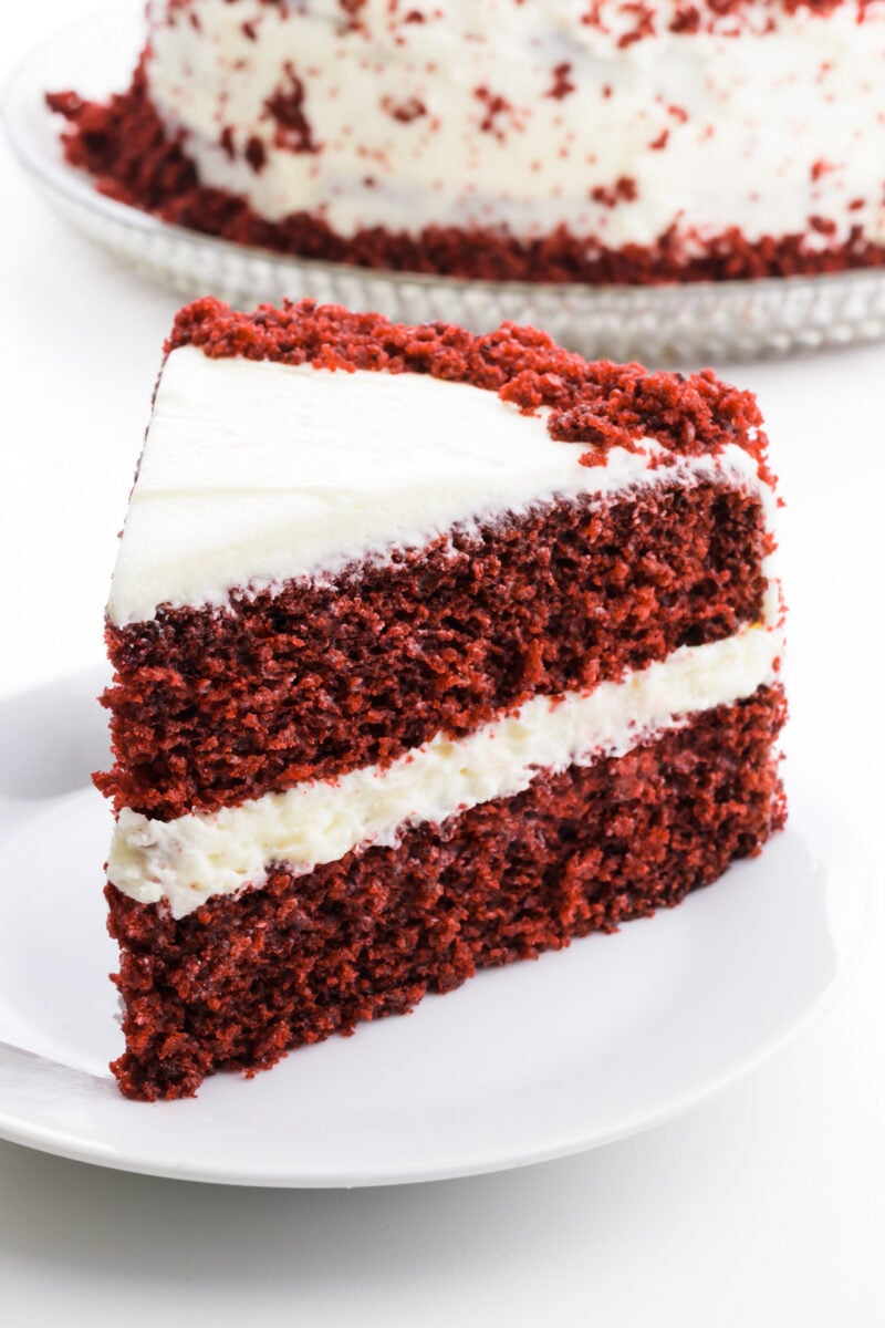 A slice of red velvet cake sits in front of the rest of the cake.