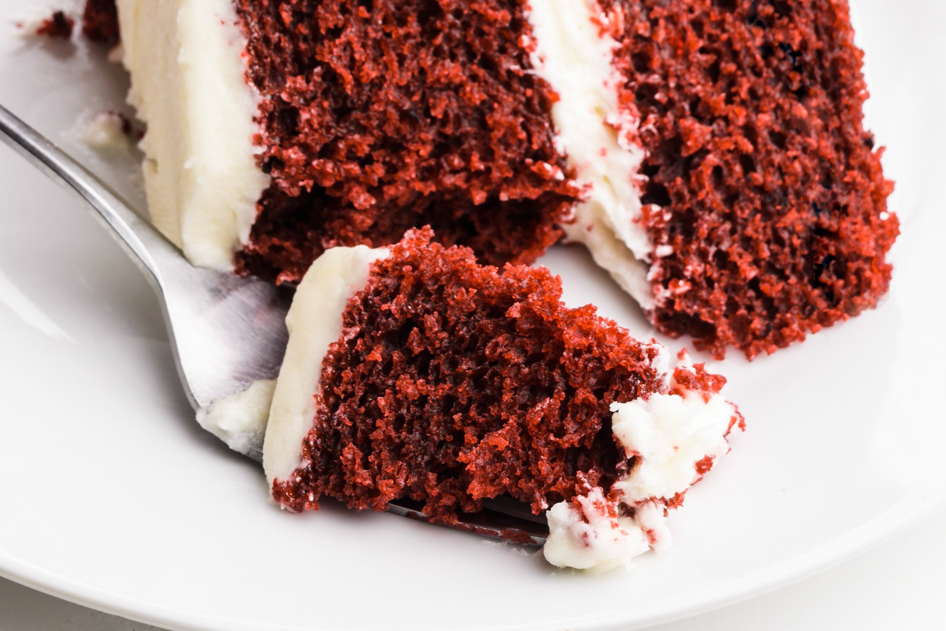 A bite of cake on a fork sits in front of the rest of the cake.
